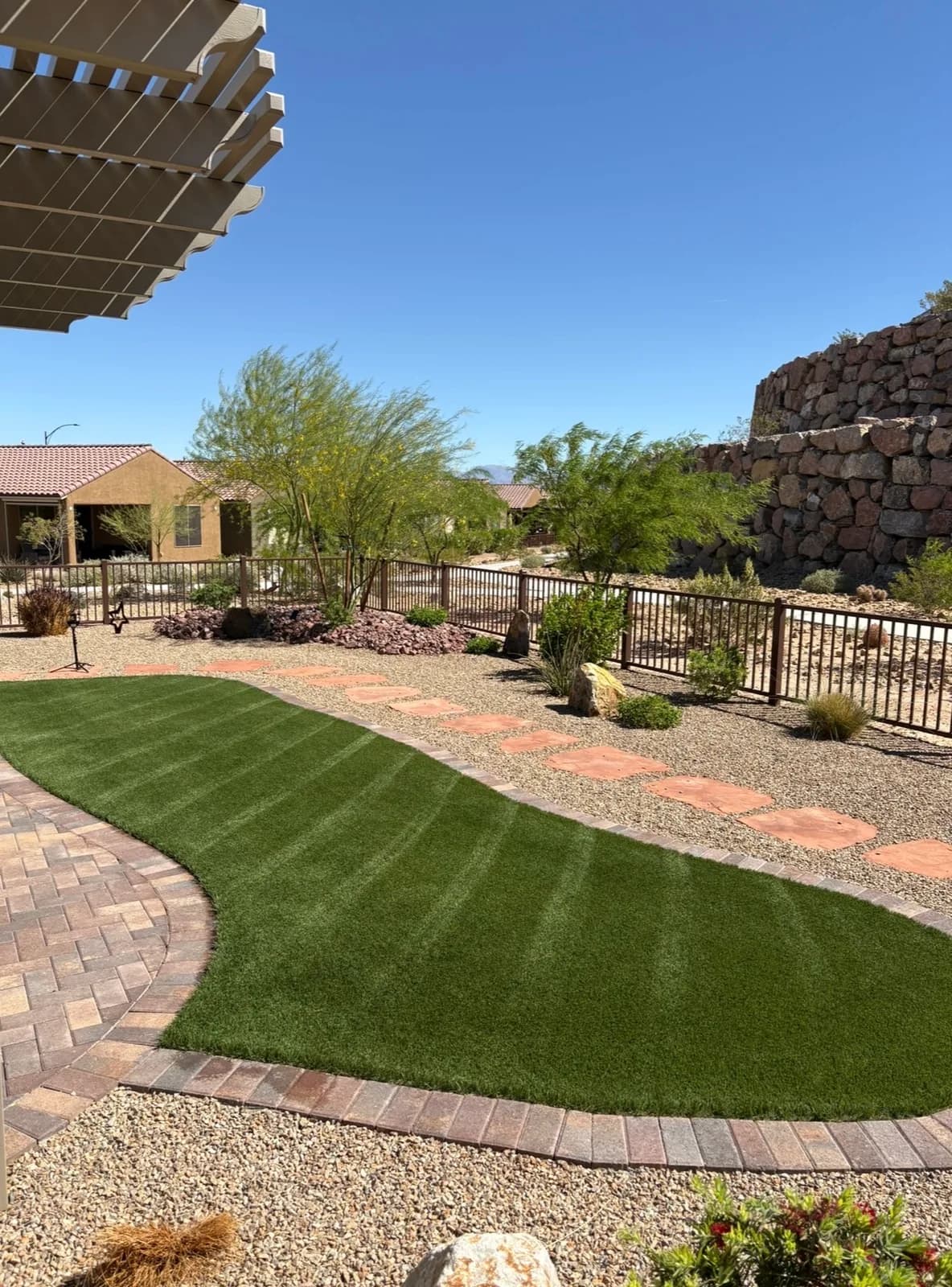 Curved artificial turf island with upright green fibers, bordered by brick pavers and decomposed granite, in a desert-landscaped backyard in Mesquite, NV.
