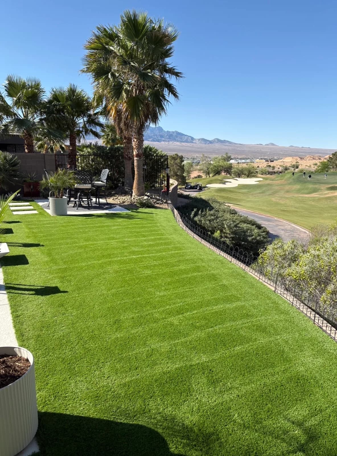 Clean, bright green artificial turf backyard with palm trees and patio furniture, overlooking a golf course fairway in Mesquite, NV after deep turf cleaning.