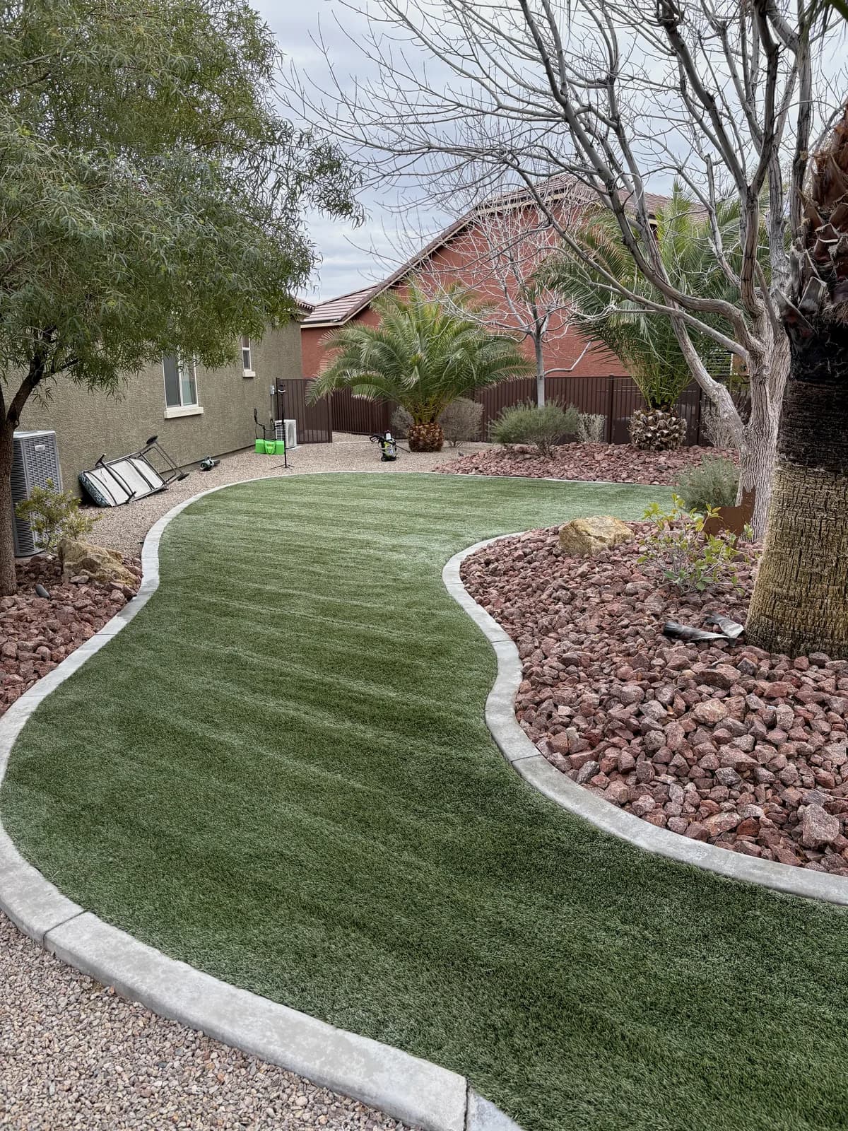 Side yard artificial turf restored to upright vibrant green next to red rock borders and a residential patio