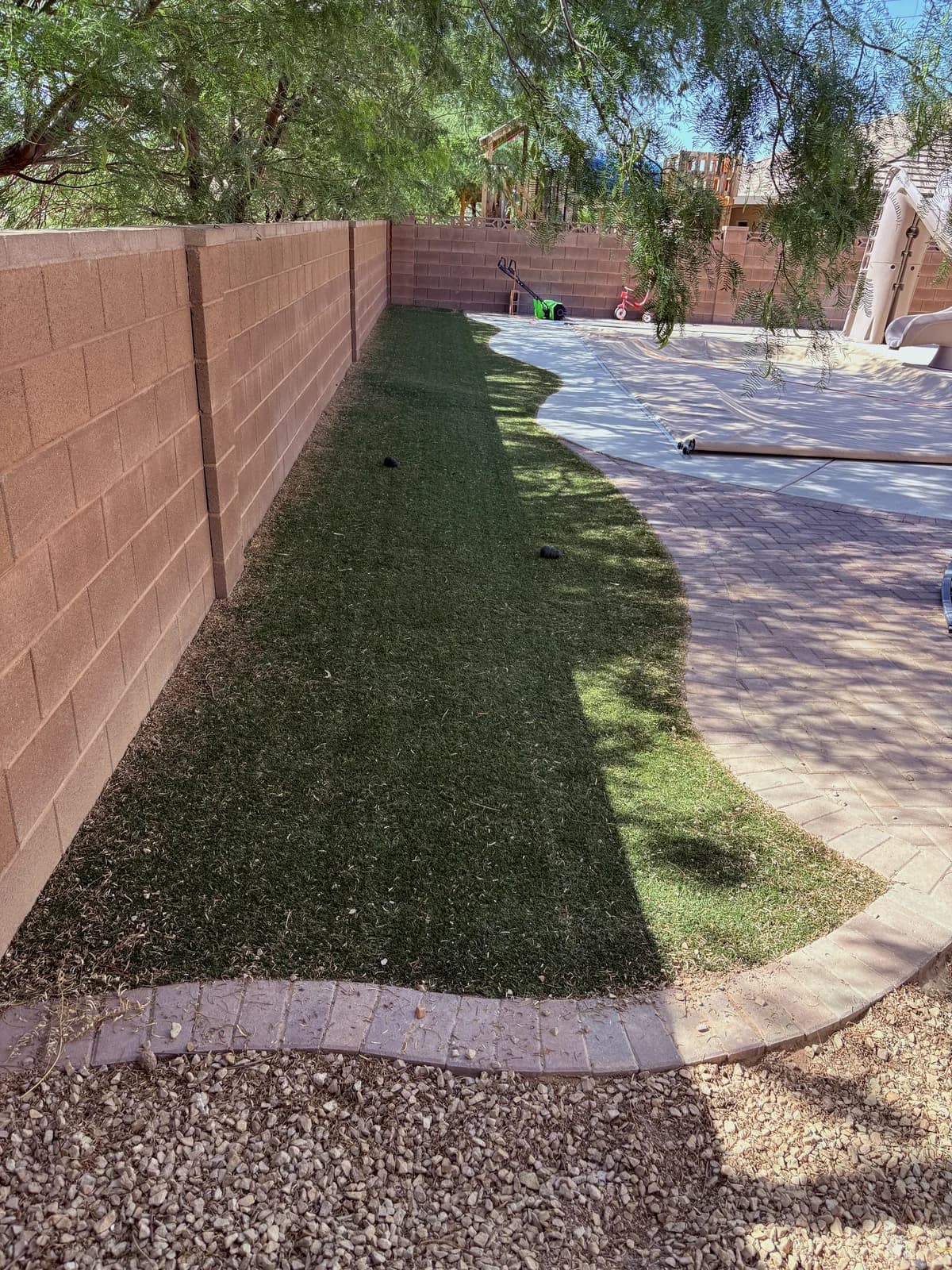 Narrow side yard artificial turf strip cleaned of fine debris and leaves along a block wall