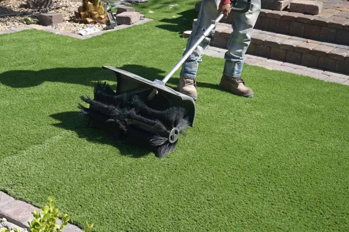 Operator running a Turfmatic power broom across artificial turf during a recurring maintenance visit