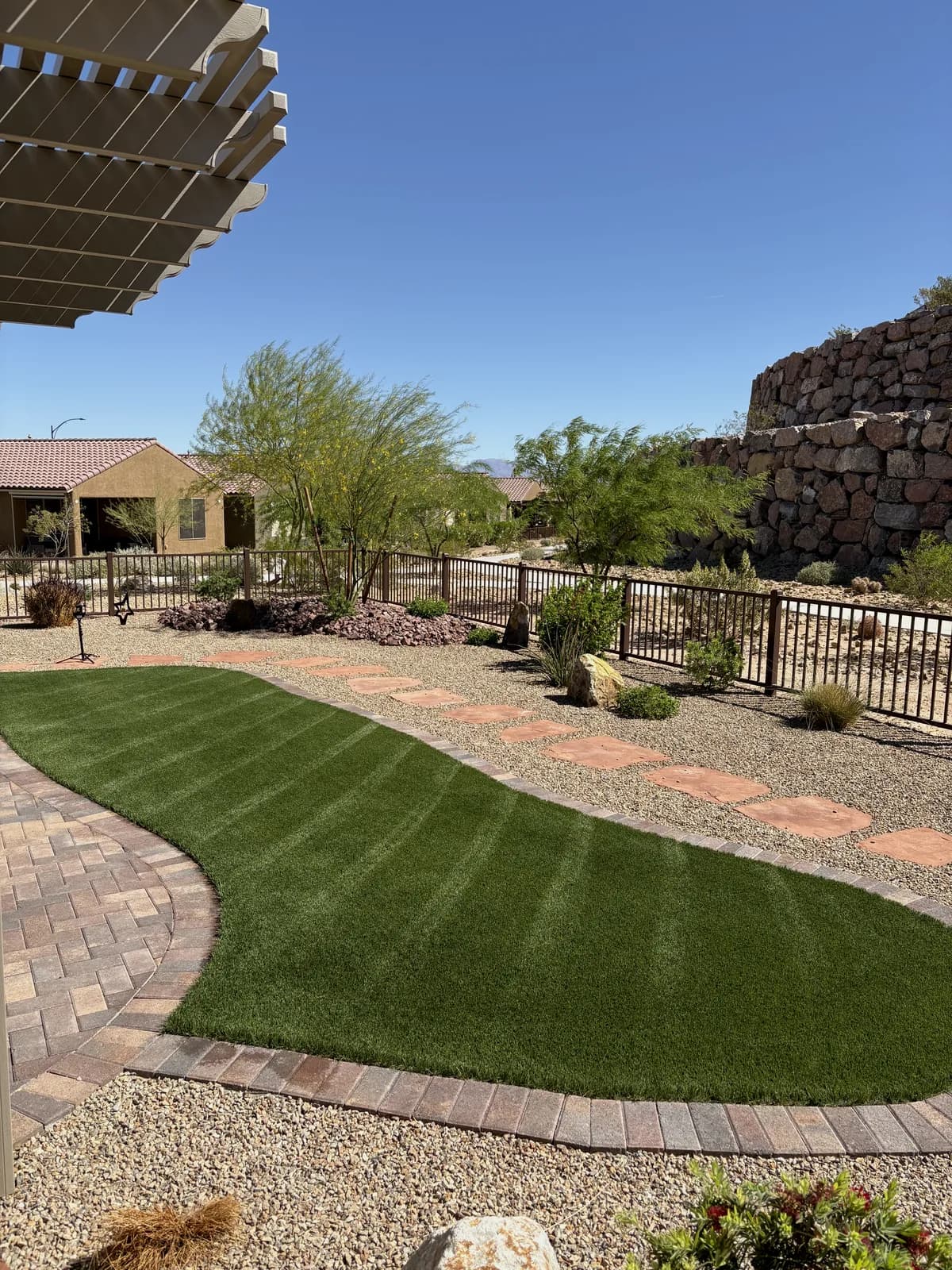 Sanitized artificial turf walkway curving through a desert garden with stacked rock retaining wall